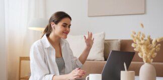 Cheerful young woman using laptop for a video call in a cozy living room, feeling connected and happy via pexels